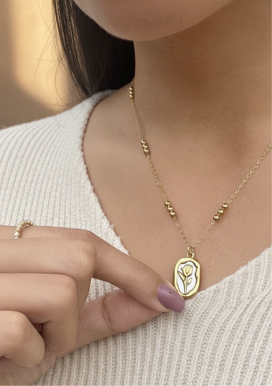 Lilyah Jewelry Necklace. Rose or Tulip
Gold necklace with a pendant worn by a person, with a blurred background.