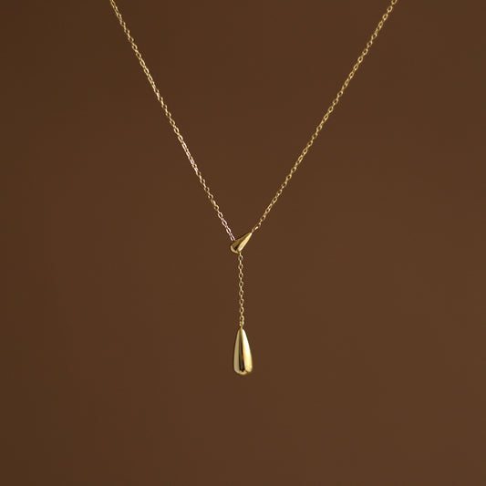 A gold-plated dainty water droplet necklace on a brown background. Lilyah Jewelry Gold Plated Necklace. Gift Ideas for her.