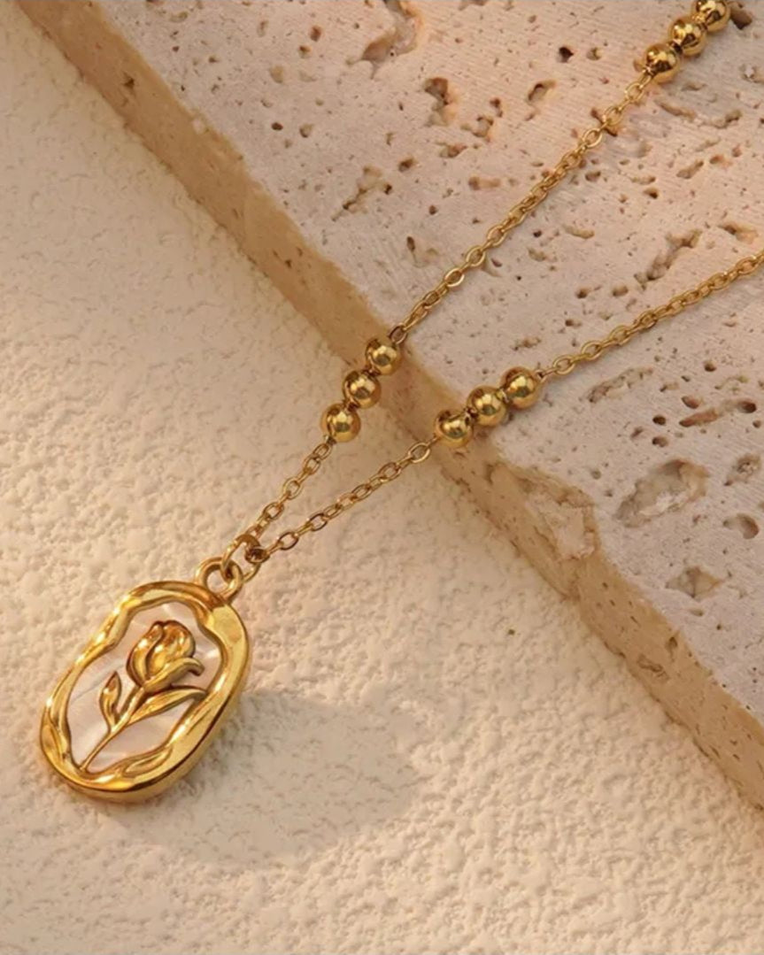 Lilyah Jewelry Necklace. Rose or tulip Gold necklace with a pendant on a textured beige surface
