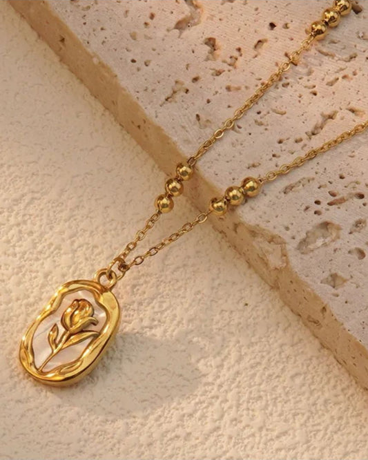 Lilyah Jewelry Necklace. Rose or tulip Gold necklace with a pendant on a textured beige surface