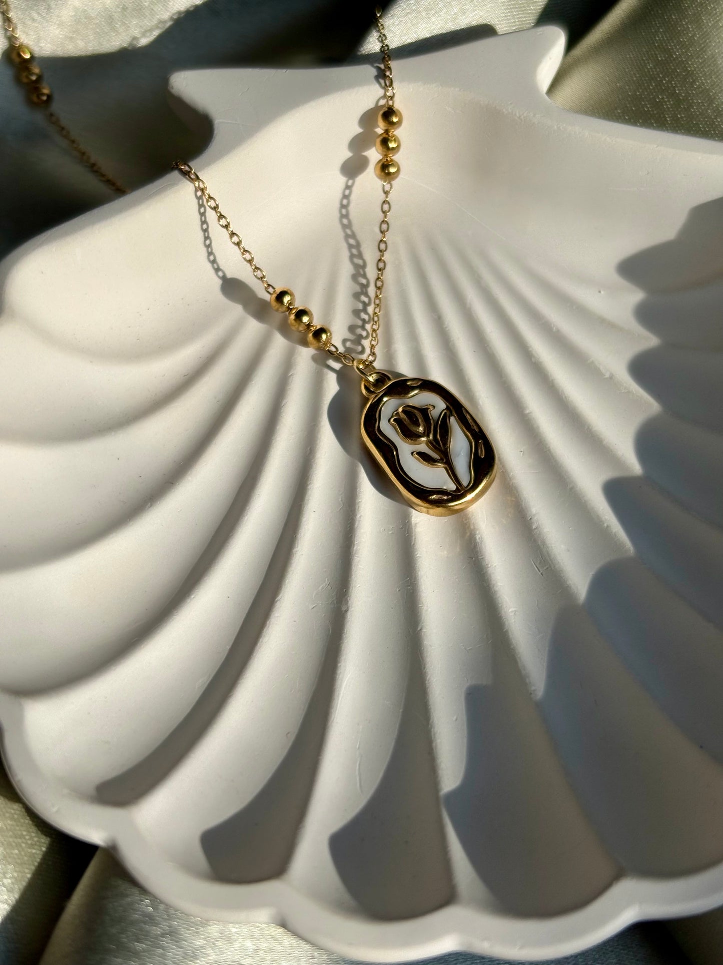 Lilyah Jewelry Necklace. Gold necklace with a pendant on a white shell under sunlight