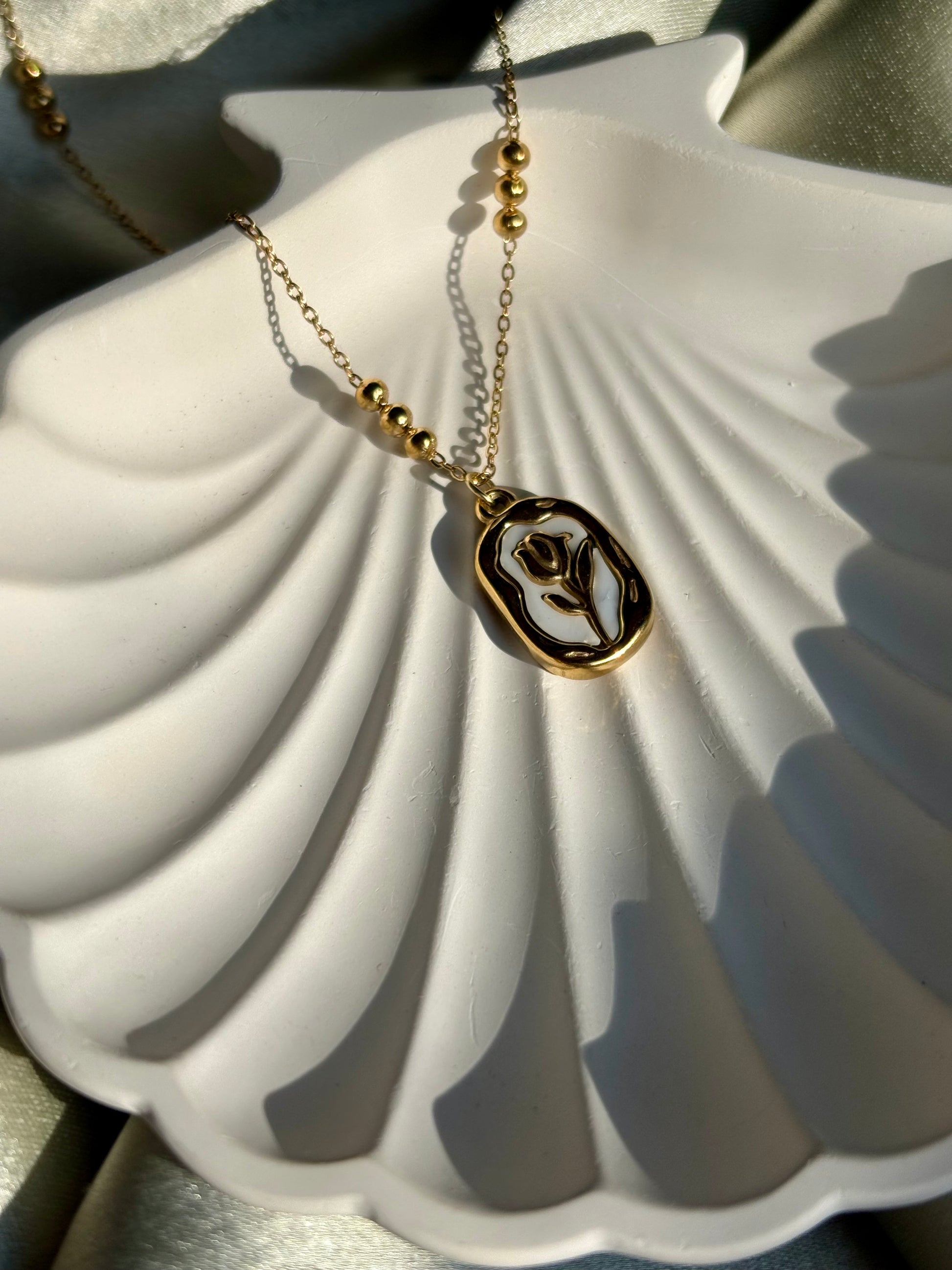 Lilyah Jewelry Necklace. Gold necklace with a pendant on a white shell under sunlight