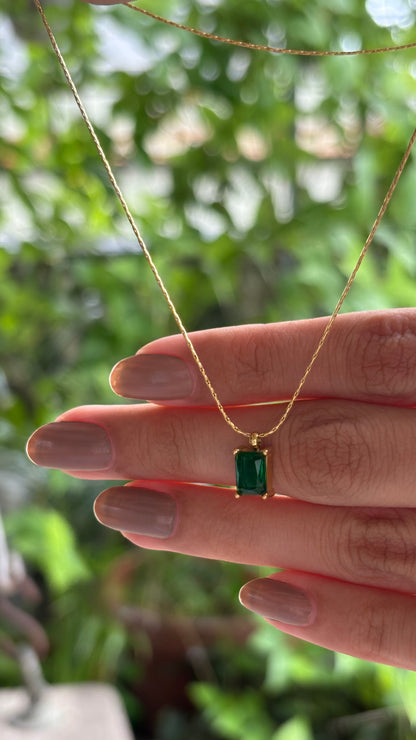 Gold necklace with an emerald pendant held by a hand against a blurred green background. Lilyah Jewelry Gold Plated Necklace. Gift Ideas for her.