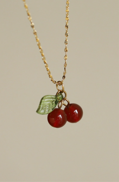 Lilyah Jewelry gold plated Necklace with cherry and leaf charm on a beige background