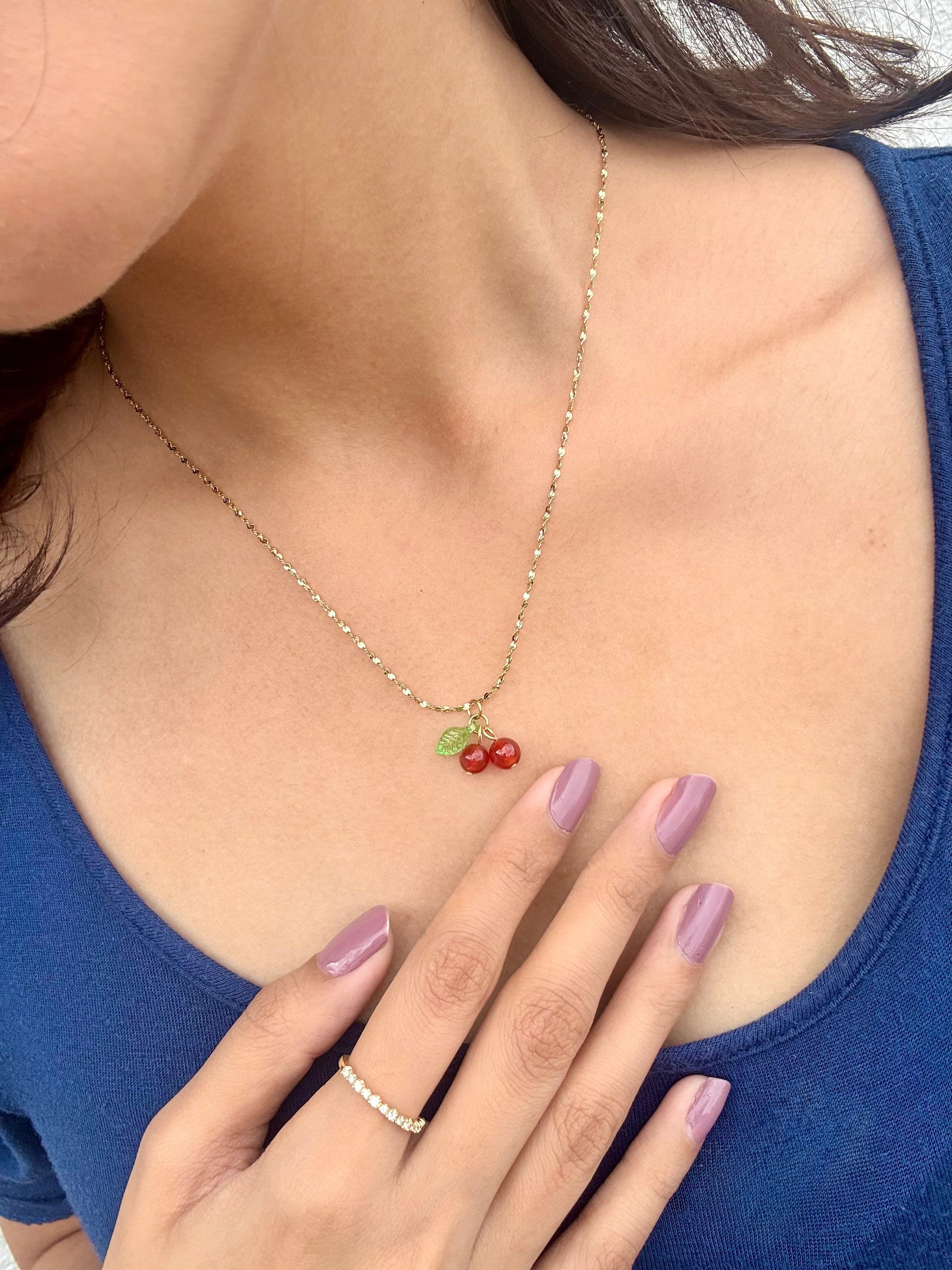 Lilyah Jewelry gold plated Necklace. Person wearing a necklace with cherry pendants, hand on chest, blue top