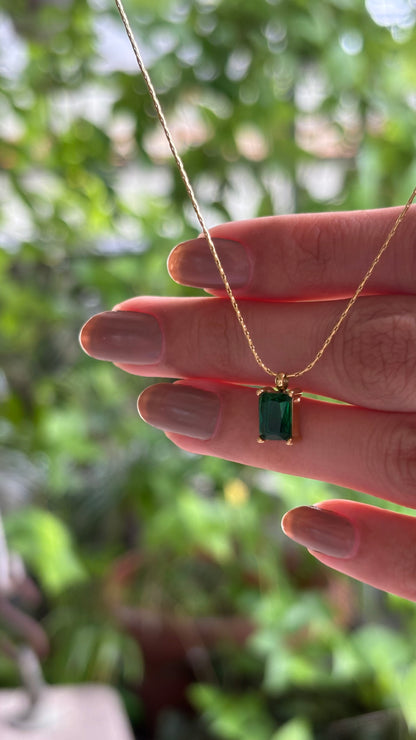 Gold necklace with a green gemstone pendant held by a hand against a blurred green background. Lilyah Jewelry Gold Plated Necklace. Gift Ideas for her.