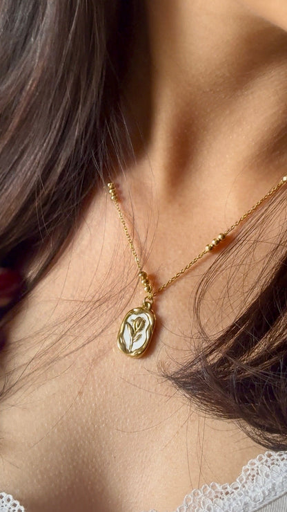 Close-up of a gold necklace with a rose pendant worn by a person.