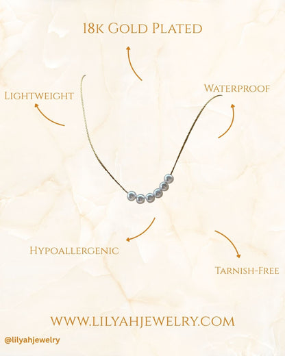 Pearl necklace with gold plating on a light beige background, featuring text about product features - it is 18k gold plated, waterproof, lightweight, tarnish free and hypoallergenic.