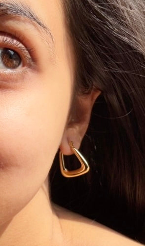 A close-up image of a woman's ear wearing a gold-plated triangular hoop earring. Lilyah Jewelry Gold Plated Earring. Gift Ideas for her.