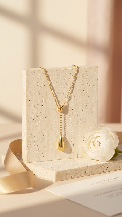 Lilyah Jewelry's Gold plated necklace on a beige stand with a white rose and ribbon. The necklace looks like it has two golden drops. It is adjustable, minimal yet a statement piece.