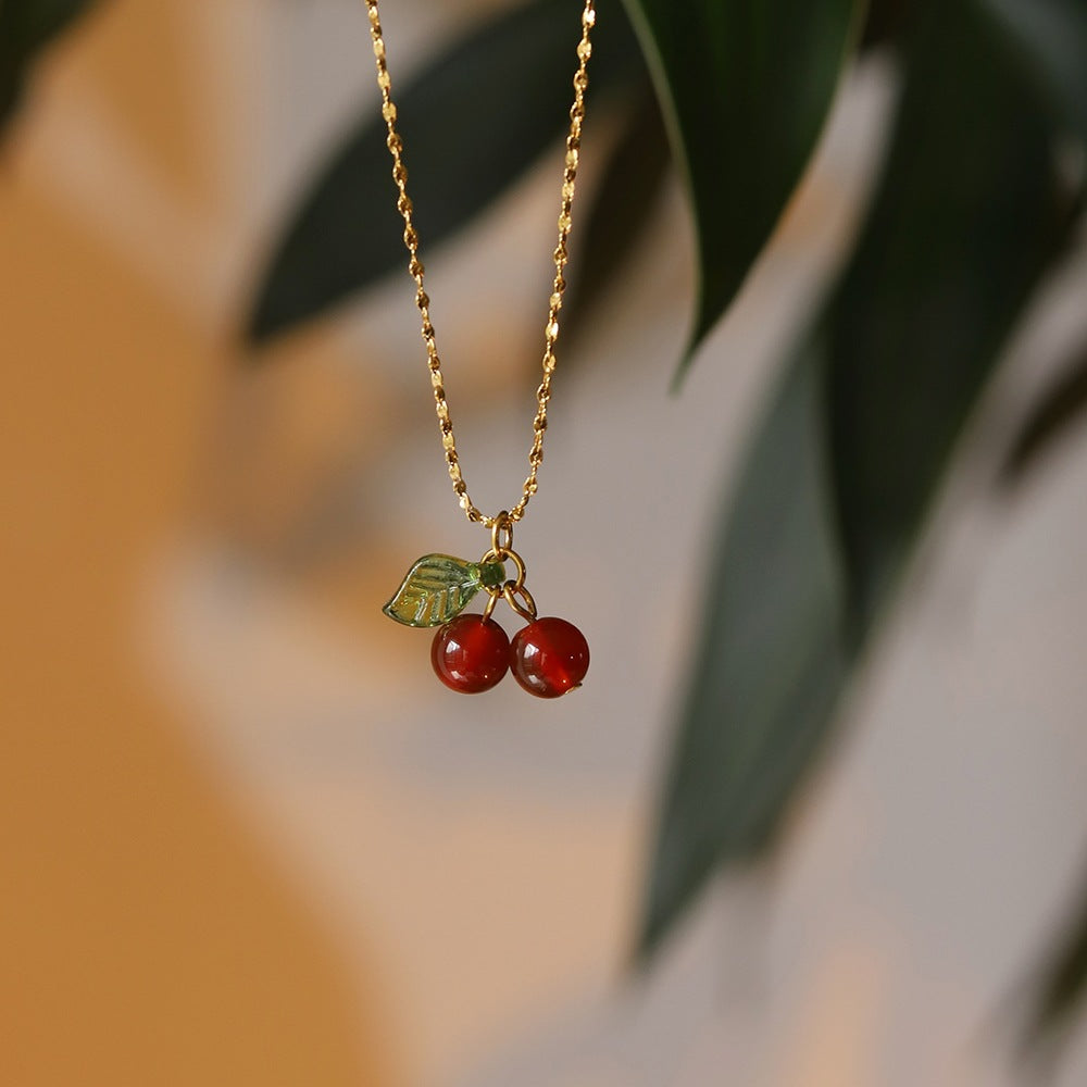 Lilyah Jewelry Necklace. Gold plated necklace with red berry pendants against a blurred natural background