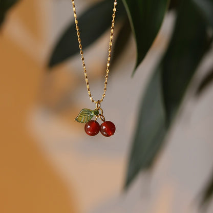 Lilyah Jewelry Necklace. Gold plated necklace with red berry pendants against a blurred natural background
