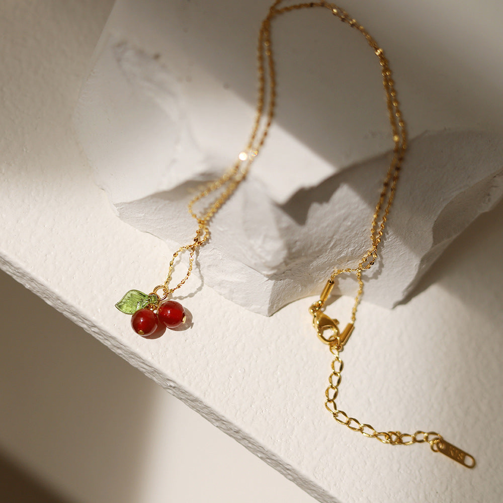 Lilyah Jewelry Necklace. 
Gold plated necklace with cherry pendant on a textured white surface