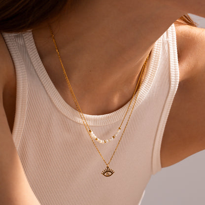 A person wearing a white tank top, showcasing a gold-plated evil eye double-layer necklace. Lilyah Jewelry Gold Plated Necklace. Gift Ideas for her.