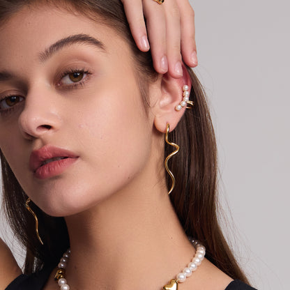 A person wearing gold-plated squiggle drop earrings and other jewelry, with a focus on the earrings. Lilyah Jewelry Gold Plated Earring. Gift Ideas for her.