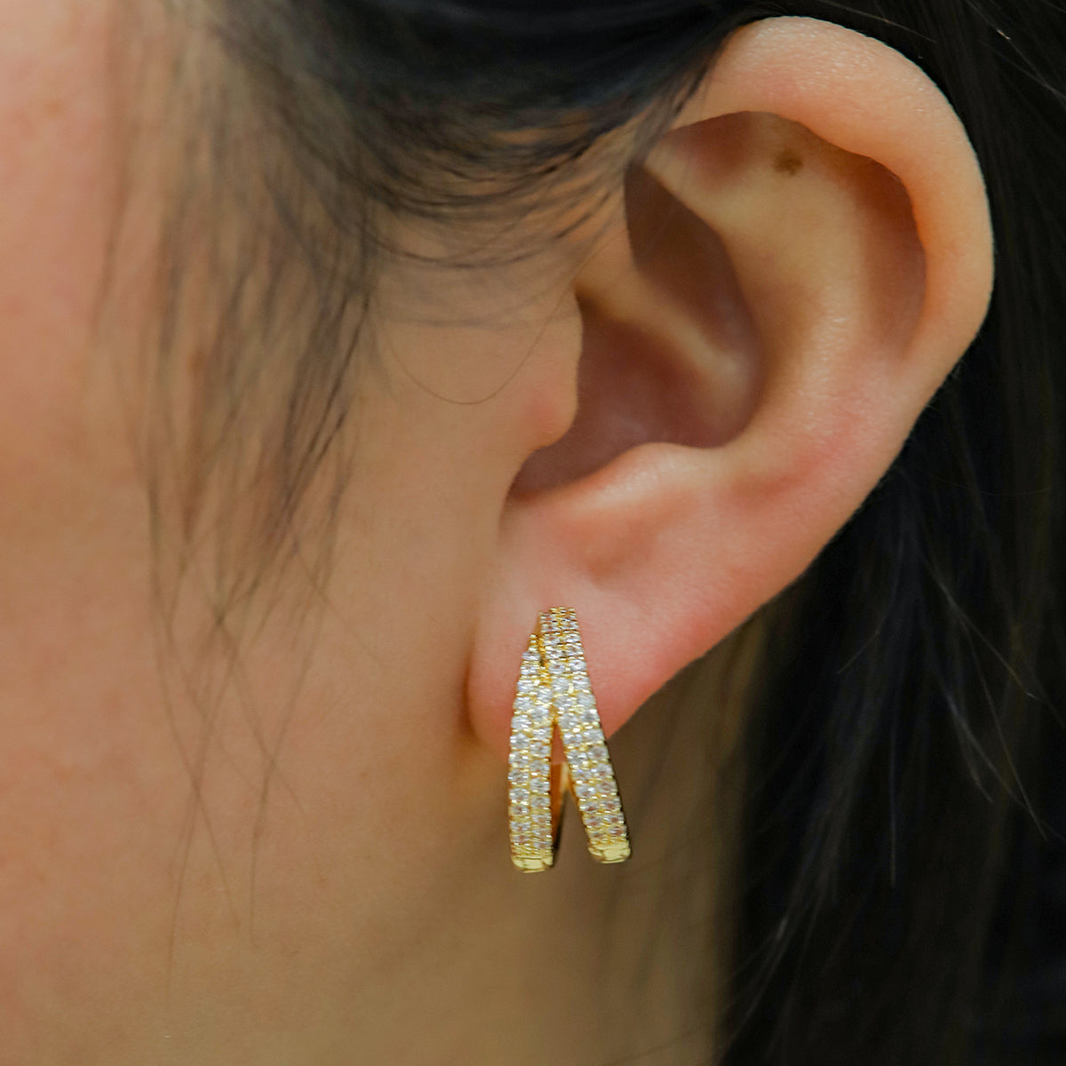 Lilyah Jewelry Gold Plated Earrings.  Close-up of an ear wearing gold plated zircon diamond hoop earrings with a blurred background