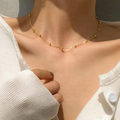 A close-up image of a woman wearing a white v-neck sweater, with a focus on a gold-plated stardust bead necklace. Lilyah Jewelry Gold Plated necklace. Gift Ideas for her.