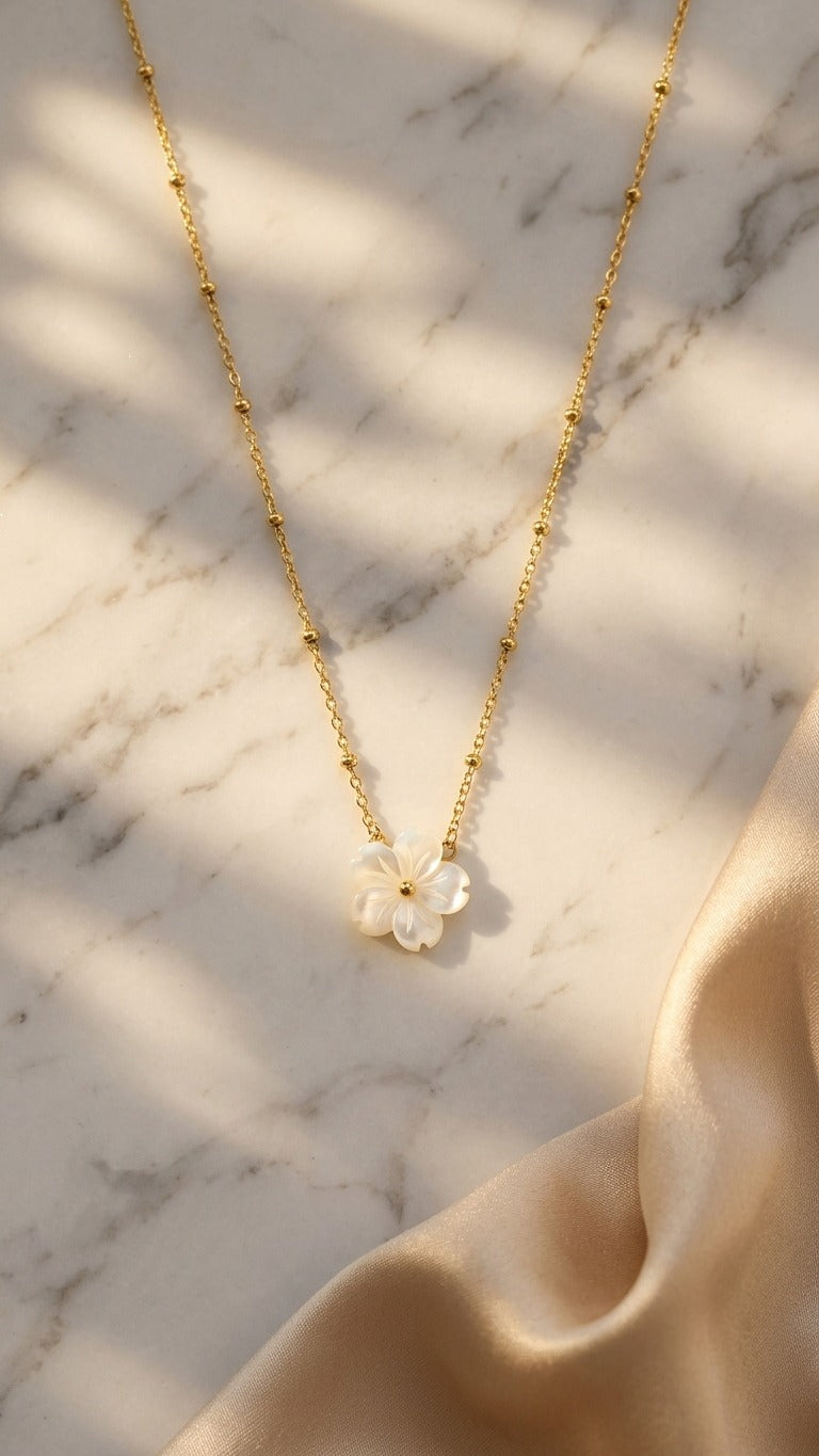 Gold necklace with a floral pendant on a marble surface with soft natural lighting