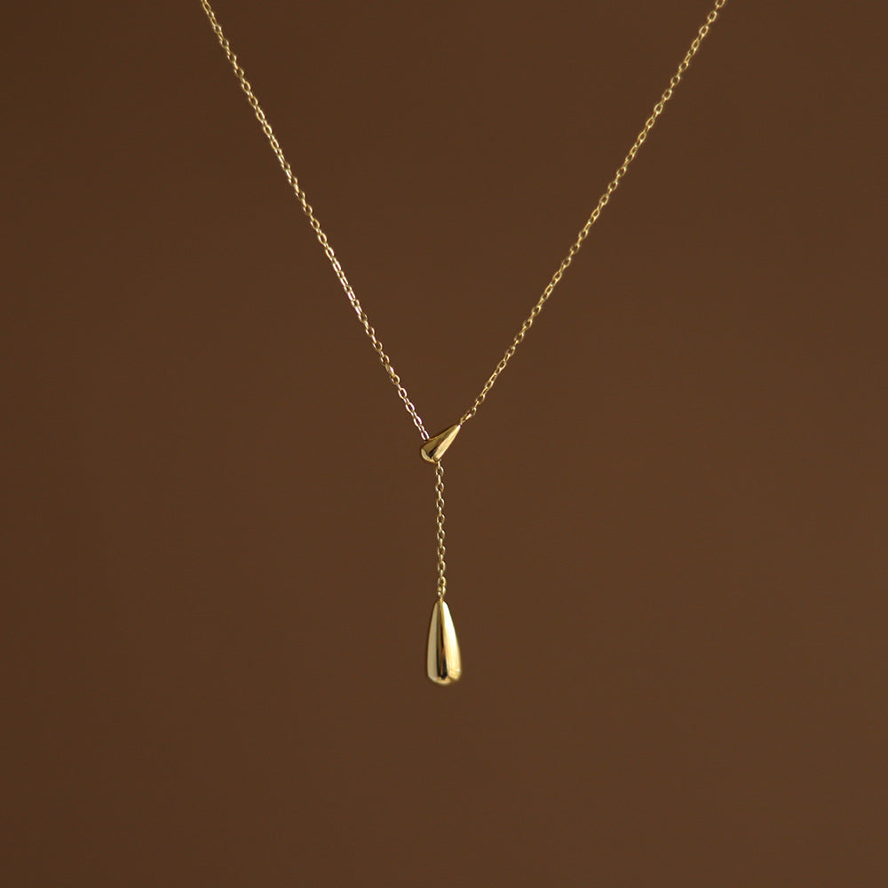 A gold-plated dainty golden water droplet necklace on a brown background. Lilyah Jewelry Gold Plated Necklace. Gift Ideas for her.